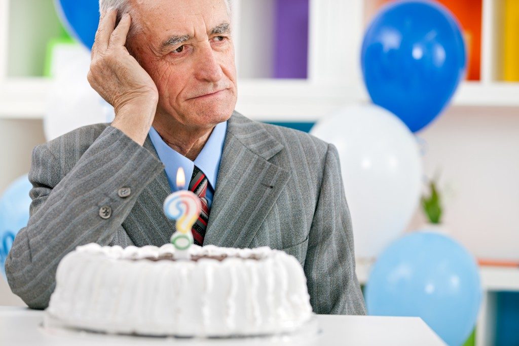 Senior man sitting front of birthday cake and trying to remember how old is
