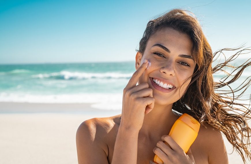 woman at the beach applying sunscreen on her face