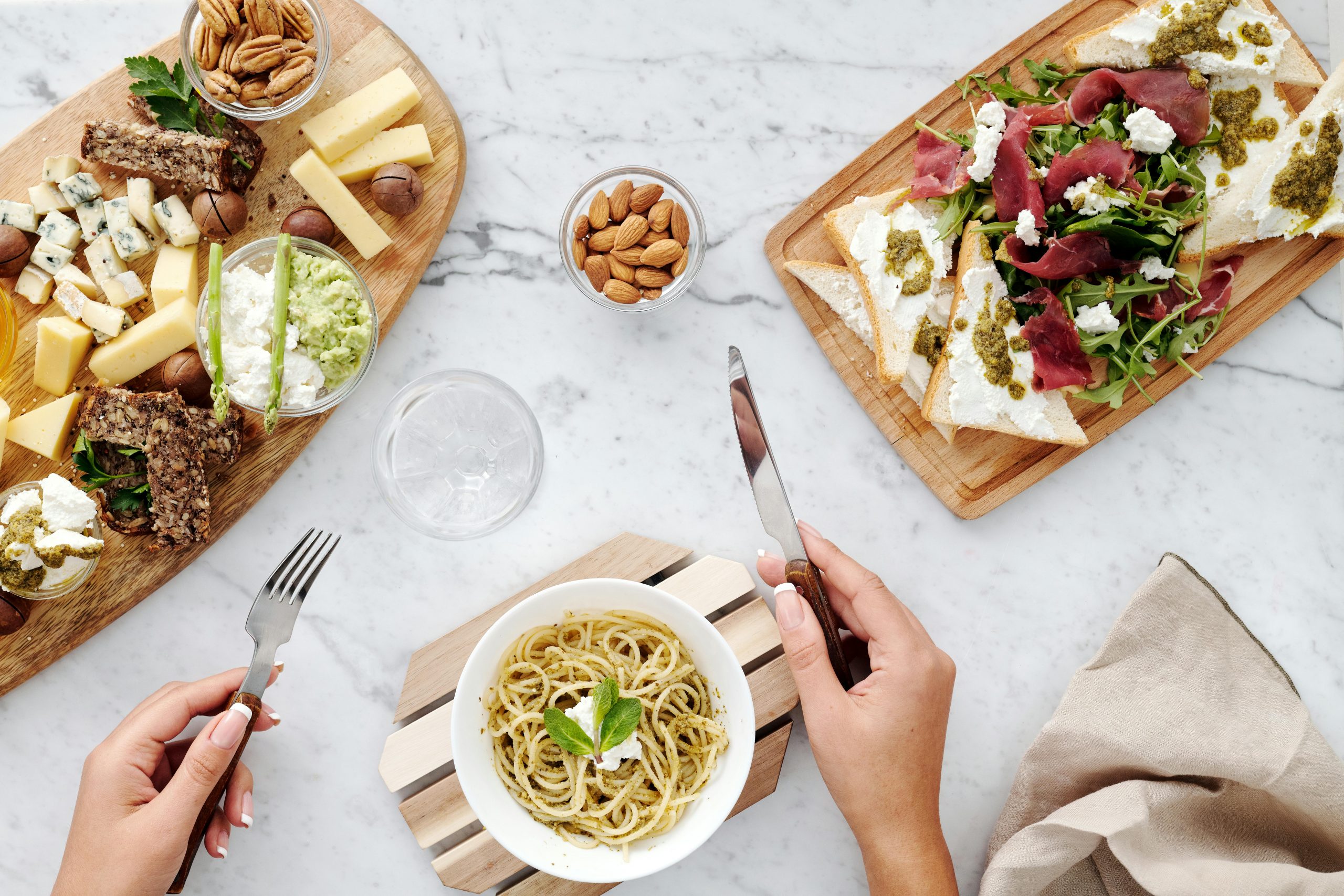 hands with a french tip manicure holding a knife and a fork at a table set with healthy dishes and a glass of water