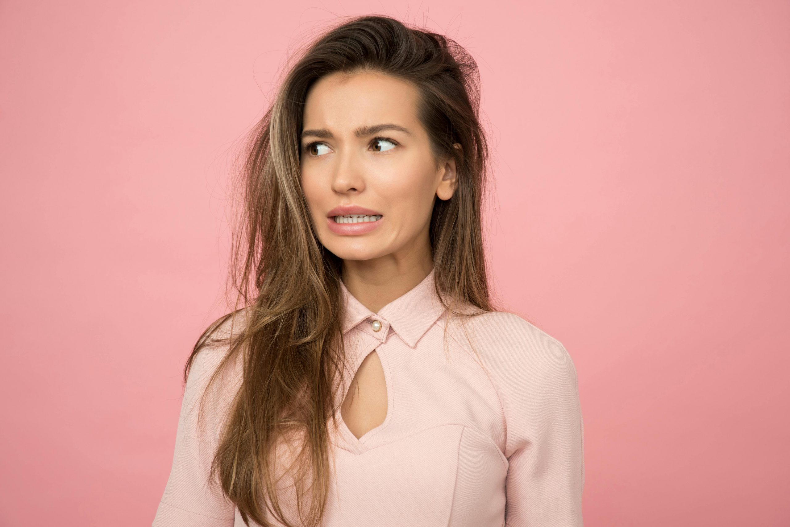 woman wearing a pink top, looking to the side with clenched teeth, appearing tense