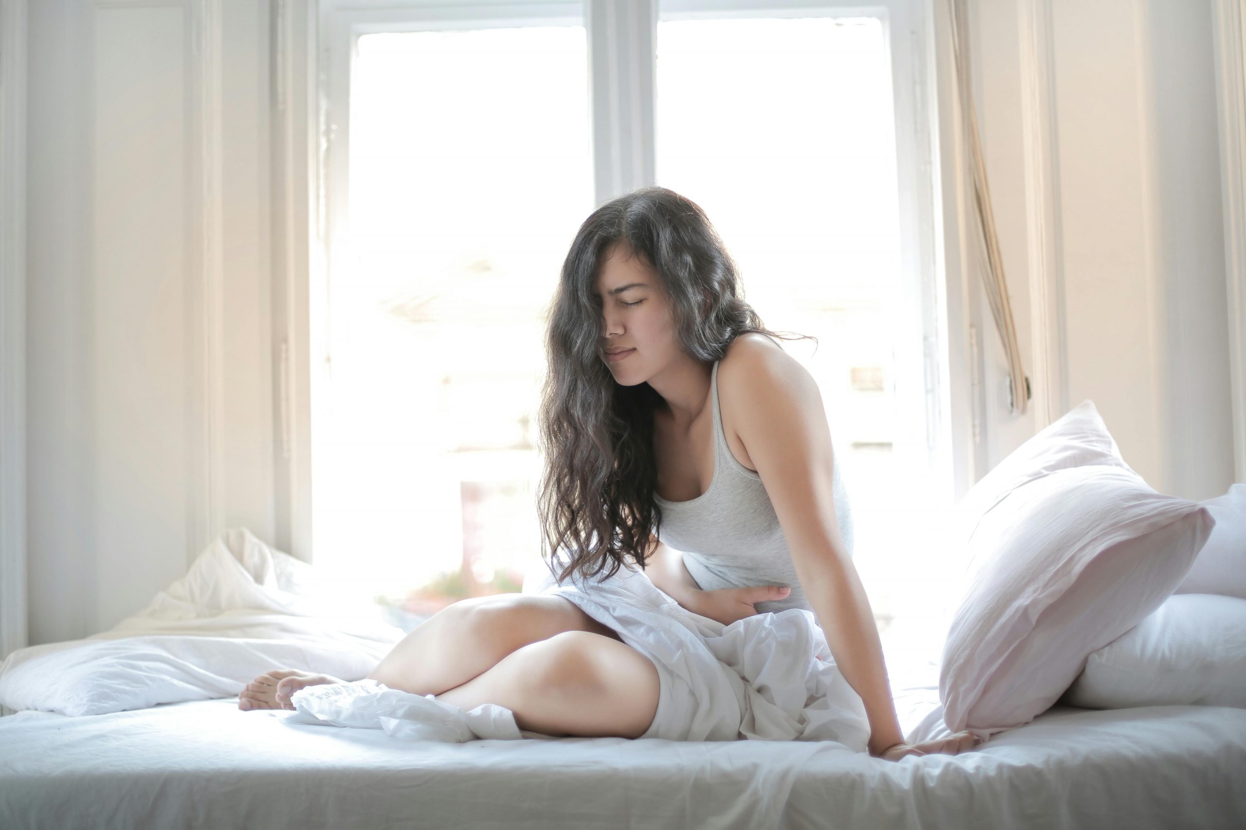 woman sitting on her bed with one hand on her lower abdomen