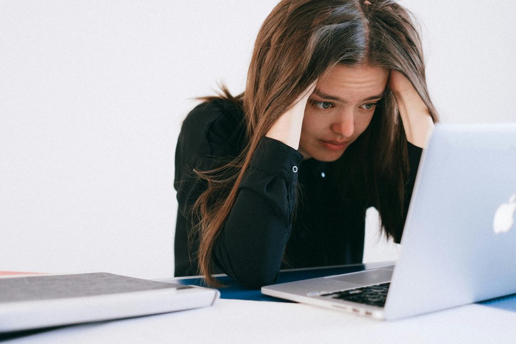 stressed woman with hands on her head, looking at a computer screen