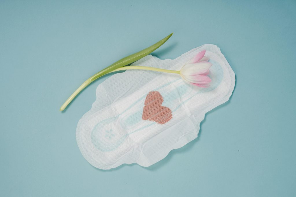 menstrual pad with pink menstrual blood shaped into a heart, with a pink flower placed on top